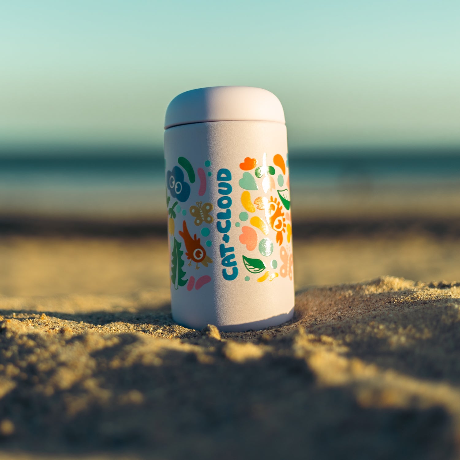 Cat & Cloud Summer Tumbler in the sand on a beach with logo visable